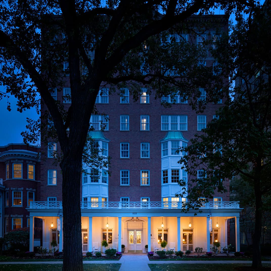 Graduate Evanston at dusk, its porch lit beneath the trees